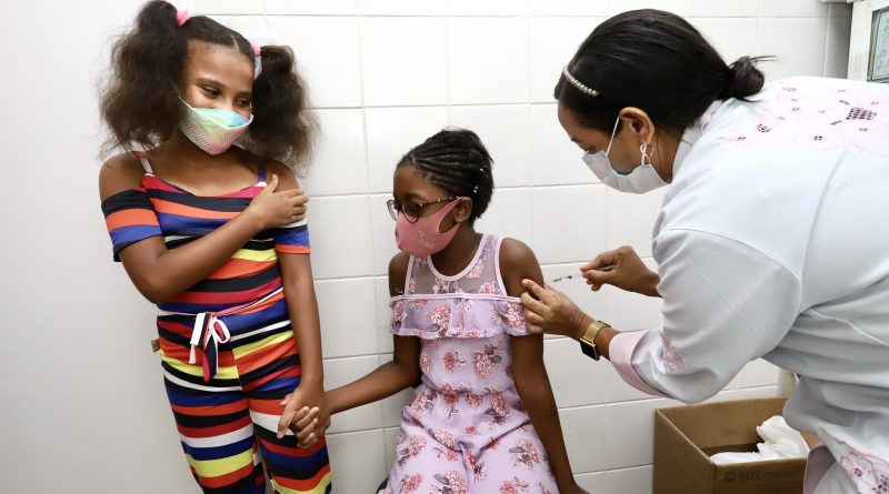 Nesta segunda-feira (24), a vacinação infantil contra a Covid-19 continua em Lauro de Freitas para os pequenos sem comorbidades com idade entre 08 a 11 anos, das 8h às 12h, na Unime, na Avenida Luís Tarquínio, e na Escola Dois de Julho, na Itinga. Para receber a proteção é necessário estar cadastrado, apresentar documento de identificação, cartão SUS ou CPF, comprovante de residência, além do formulário de autorização que pode ser impresso através do site da prefeitura -www.laurodefreitas.ba.gov.br ou estará disponível para preenchimento no próprio local de vacinação. Também nesta segunda-feira (24), adultos ou adolescentes que precisam tomar a 2ª dose da Astrazeneca ou Jansen podem tomar a vacina no Ginásio de Esportes do Aracuí ou Quadra do Colégio Dois de Julho, na Itinga, também das 8h às 12h. Para a 2ª dose é necessário apresentar documento de identificação e cartão de vacina com a primeira dose. A vacinação de para a 1ª e 3ª dose estará suspensa nesta segunda. Chuva não atrapalhou Nem mesmo a chuva forte que caiu na manhã deste domingo (23), em Lauro de Freitas, foi capaz de evitar que pais e responsáveis levassem os pequenos para se vacinarem contra a Covid-19. Crianças com idade entre 09 e 11 anos e crianças com comorbidades de 5 a 11, compareceram a Unidade de Saúde da Família São Judas Tadeu, na Itinga, De acordo com o secretário municipal de Saúde, Augusto César Pereira, a estratégia para aplicar a vacina no domingo foi pensada para dar possibilidade aos que não podem trazer as crianças durante a semana. "Nós estamos aplicando a vacina nos pequenos todos os dias, de segunda a sexta-feira, e separamos o domingo para aqueles que trabalham poderem vir trazer suas crianças para se protegerem. Queremos alcançar o número maior desse público vacinado em menor tempo" explicou. Apoiando-se uma no braço da outra, as amigas Natália Cristina e Vanessa Costa, uma com 9 e outra com 10 anos, foram acompanhadas pela mãe de uma das crianças, a dona de casa Meire Costa, para tomar a dose da vacina. "Eu tenho medo de agulha, mas sei que é preciso se proteger", disse Vanessa que corajosamente tomou a vacina primeiro que a amiga. Ansiosa para ver a filha protegida, Fernanda Carine Lima acompanhava diariamente o chamamento para a idade da filha se vacinar. "Nós nos mudamos para Lauro recentemente e estávamos esperando com muita expectativa este dia. Ela era a única que ainda não tinha se vacinado em casa", disse abraçando a filha, Giovanna Lima, de 10 anos. Após tomarem as doses, os responsáveis e crianças aguardam por vinte minutos numa sala reservada. A médica clínica, Bruna Oliveira, orienta enquanto os pais aguardam o tempo para liberação. "É normal após a aplicação das doses as crianças apresentarem um pouco de dor no local ou até um pouco de febre. Basta colocar compressa de água gelada e tomar analgésico de costume", disse.